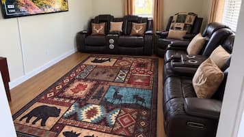 Een woonkamer met een grote flatscreen televisie, een plafondventilator en een kamerbreed tapijt met een patroon.