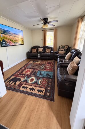 A living room with a large flat-screen TV, a ceiling fan, and a patterned rug. - Four Season Maine Retreat (Saint Francis)