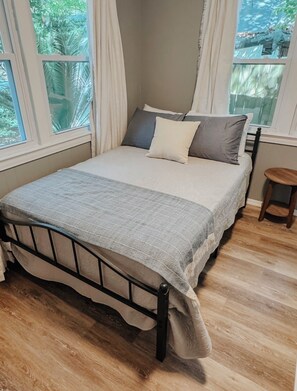 A bed with a headboard, a bedside table, and a window with curtains. - Charming 2BR Near Downtown & NAS / Pet Friendly (Pensacola)