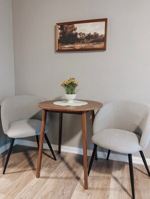 A room with two grey chairs, a small round wooden table with a white bowl of yellow flowers, and a framed painting on the wall. - Charming 2BR Near Downtown & NAS / Pet Friendly (Pensacola)