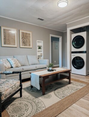 A living room with a sofa, armchair, coffee table, and a washing machine. - Charming 2BR Near Downtown & NAS / Pet Friendly (Pensacola)