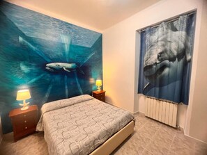 A bedroom with a bed, two nightstands, a wall mural, and a radiator. - CORALLI DI MARE 5 TERRE-JRE (La Spezia)