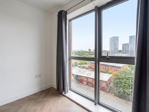 A room with a large window, a wooden floor, and a view of buildings and greenery outside. - AO Arena • Parking • Victoria Station (Manchester)