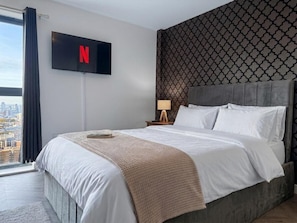 A hotel room with a bed, a TV mounted on the wall, a city view, and a patterned wall. - AO Arena • Parking • Victoria Station (Manchester)