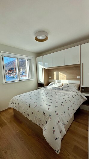 Ein Schlafzimmer mit einem großen Bett, Holzboden, einem Fenster mit Blick auf eine Baustelle und eingebauten Schränken.
