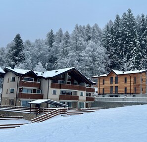 A snow-covered building with multiple balconies and a wooden facade, surrounded by snow-laden trees. - AlpenGlow SkiLodge (Corteno Golgi)