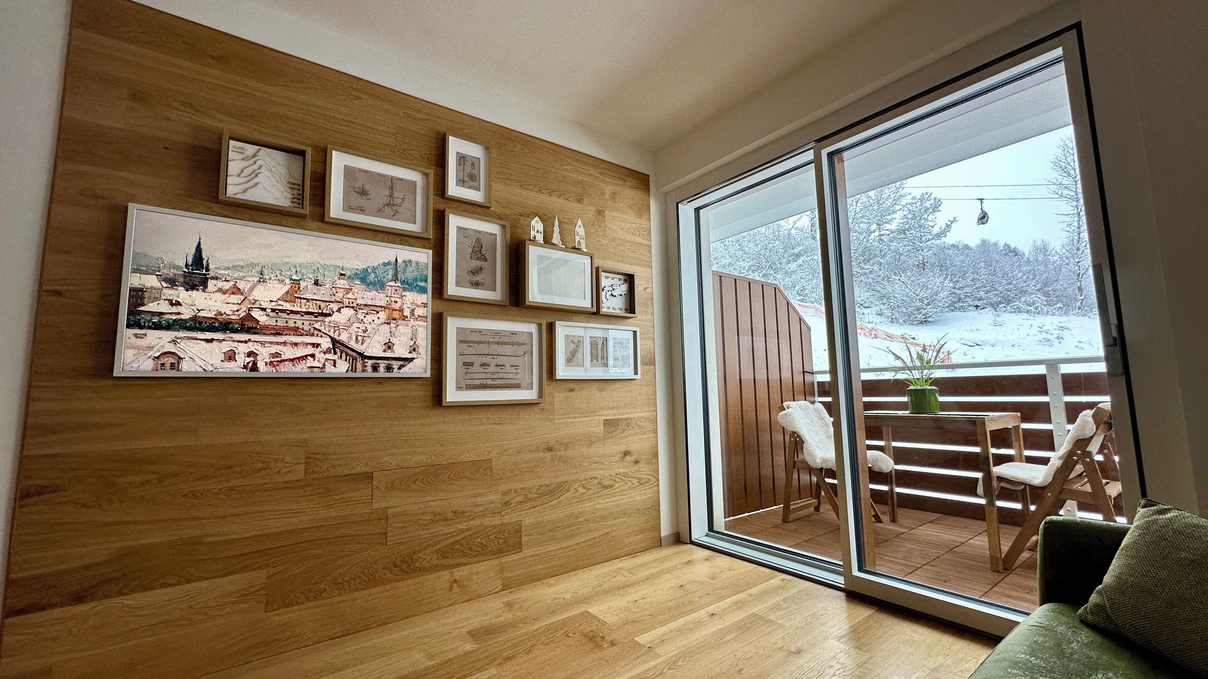 A room with a wooden wall, a large window, and various framed pictures.