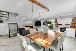 Een moderne keuken met een houten eettafel, grijze gestoffeerde stoelen en een groot raam.