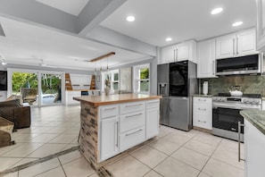 A modern kitchen with white cabinets, a central island, stainless steel appliances, and a view to the outdoors. - Family Friendly Waterfront Ft Lauderdale Retreat (Fort Lauderdale)