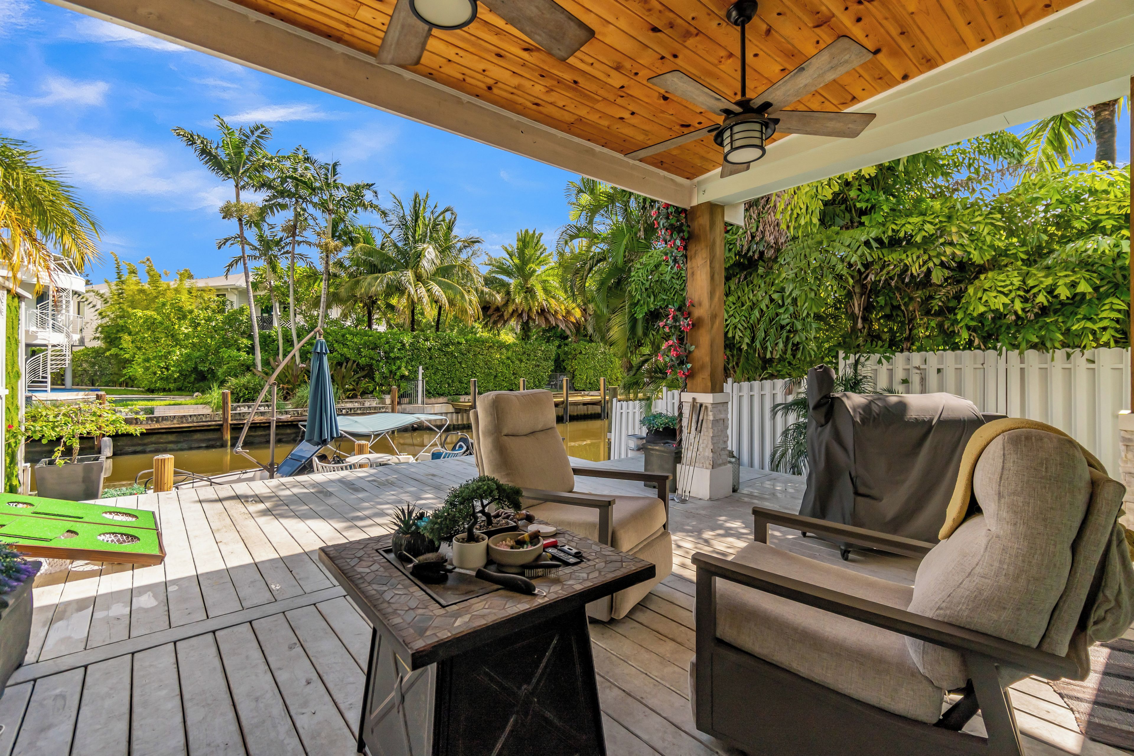 Überdachte Terrasse im Freien mit Deckenventilator, Sitzgelegenheit und Blick auf ein Wasserelement und Grünflächen.