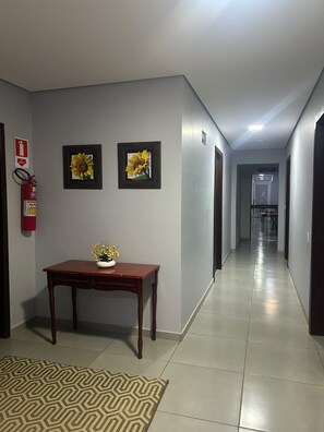 A hallway with a fire extinguisher, two framed sunflowers, a wooden table with a vase of flowers, and a patterned rug.