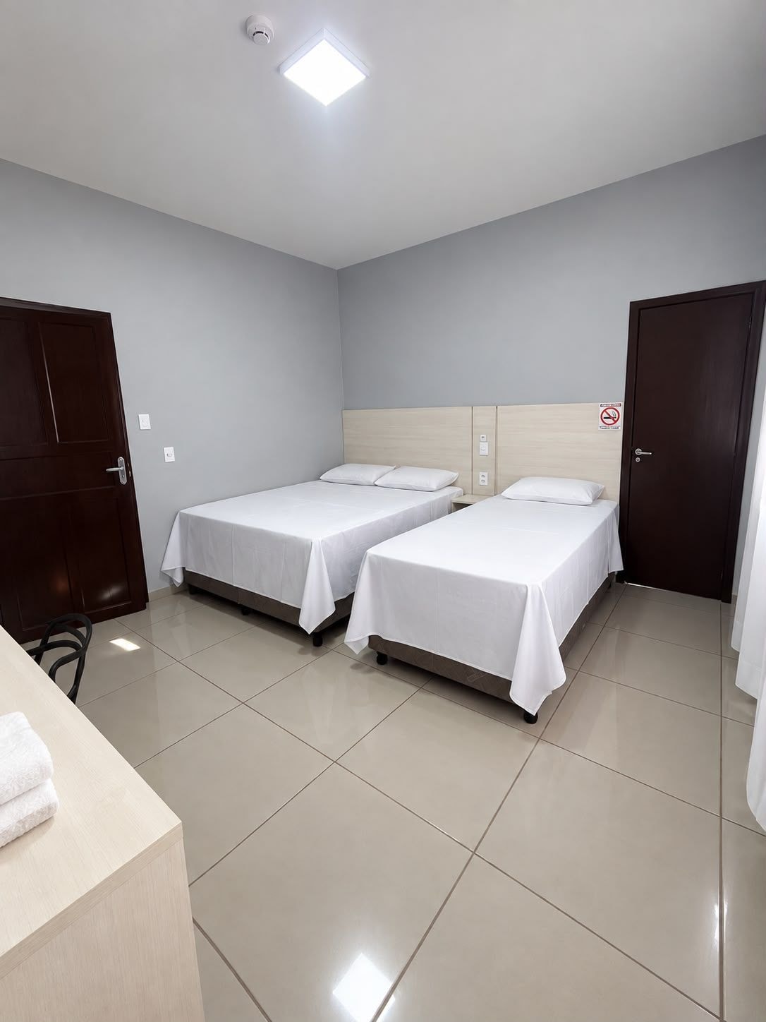 Habitación de hotel con dos camas individuales, cabecero de madera, escritorio con silla y puerta de baño.