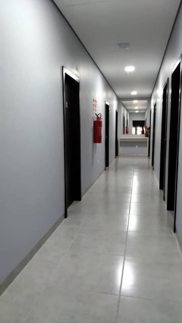 A long, narrow hallway with doors on both sides, a fire extinguisher mounted on the wall, and a clean, tiled floor. - HOTEL VIZON II (Vilhena)
