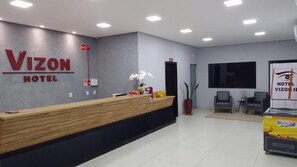 A hotel reception area with a reception desk, a plant, and a wall-mounted sign.