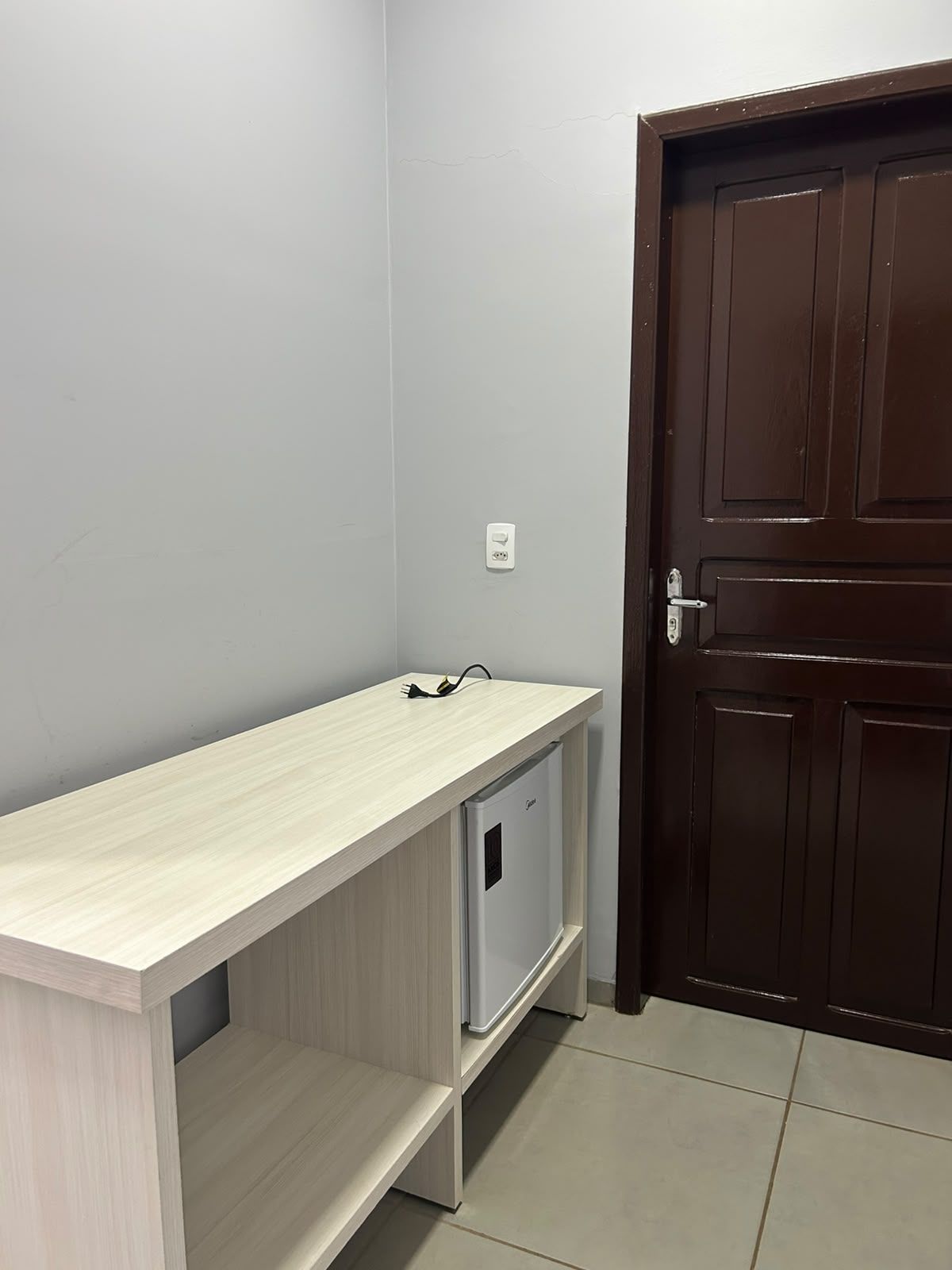 A room with a light-colored desk, a dark brown door, and a white electrical outlet.