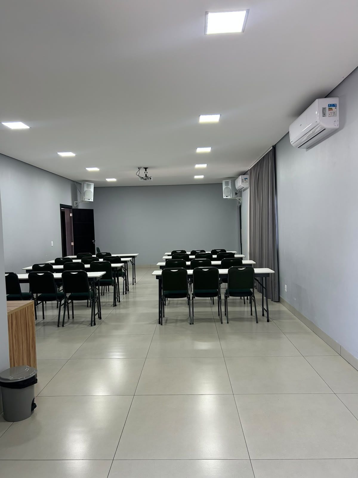 A conference room with tables and chairs, a projector, and an air conditioning unit.