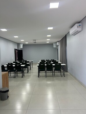 A conference room with tables and chairs, a projector, and an air conditioning unit.