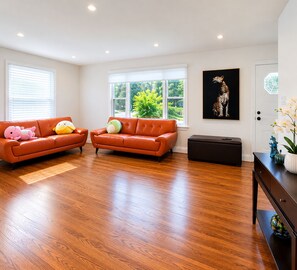 A spacious living room with two orange leather sofas, a wooden floor, and a large window with a view of greenery. - Modern 4BR Home | Subway | Parking | Toronto (Toronto)