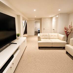 A modern living room with a flat-screen TV, a beige sofa, and a white cabinet. - Modern 4BR Home | Subway | Parking | Toronto (Toronto)