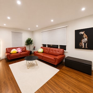 A living room with two red sofas, a black coffee table, and a leopard print artwork on the wall. - Modern 4BR Home | Subway | Parking | Toronto (Toronto)