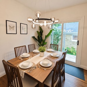 A dining room with a wooden table set for six, surrounded by chairs, a hanging light fixture, and a potted plant. - Modern 4BR Home | Subway | Parking | Toronto (Toronto)