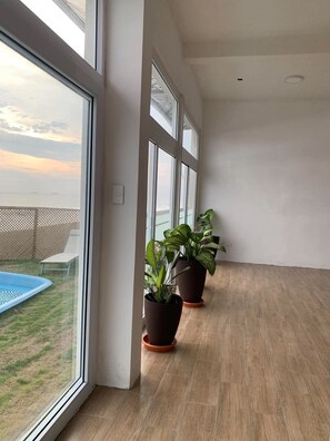 Un balcón amplio con vistas al mar, ventanas grandes y plantas en macetas.
