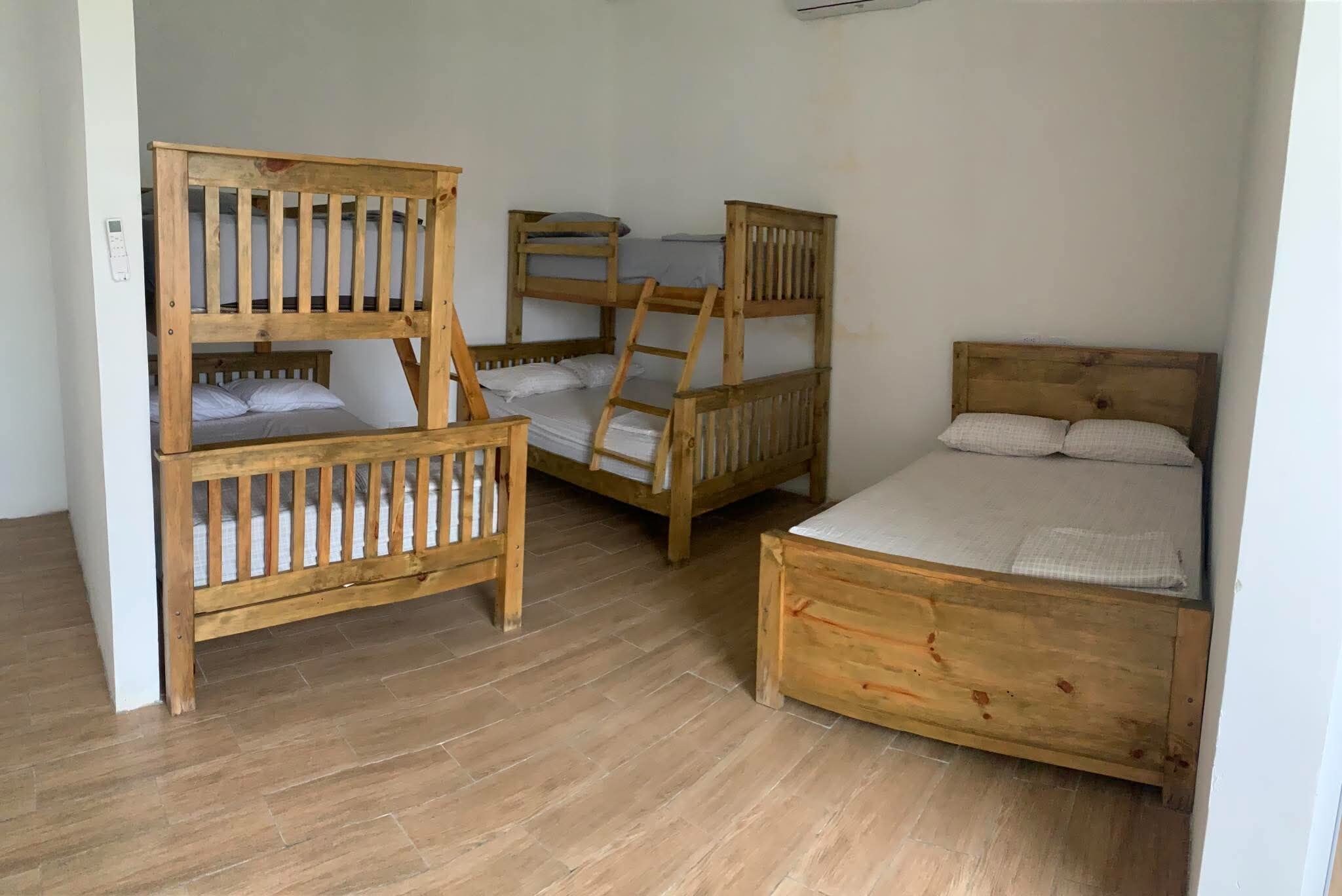A room with three wooden bunk beds and a single bed, all with white bedding.