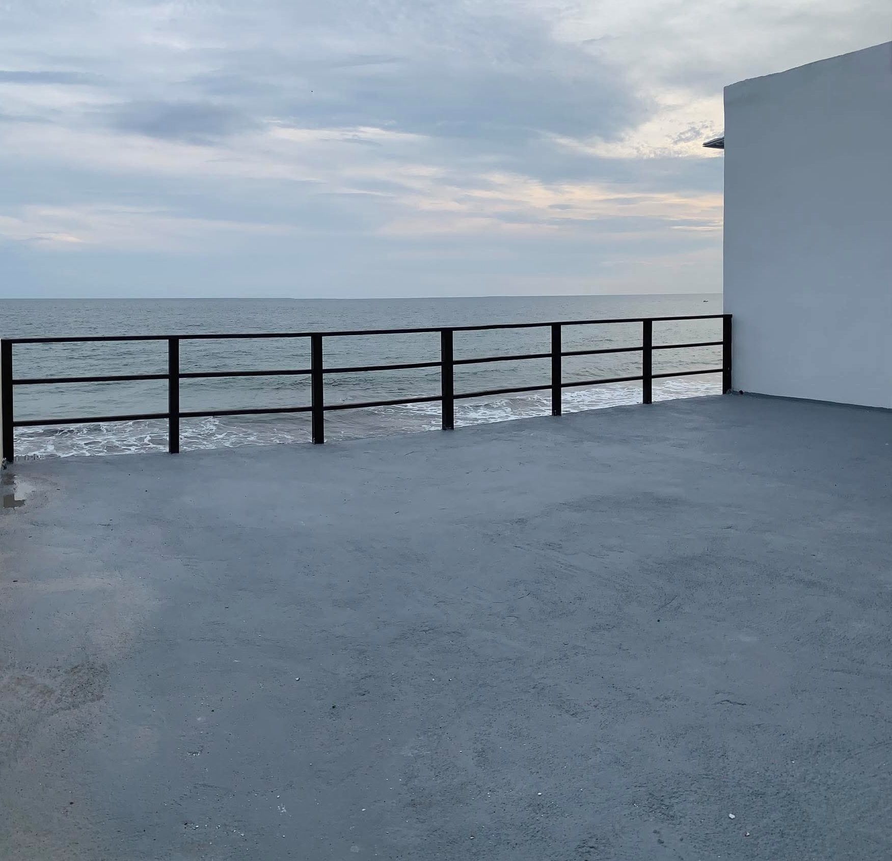 Une terrasse en béton avec une rambarde métallique donnant sur une étendue d’eau.