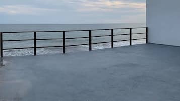 Une terrasse en béton avec une rambarde métallique donnant sur une étendue d’eau.