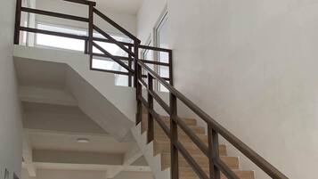 Un interior espacioso con una escalera de madera que lleva a un nivel superior, grandes ventanales con vistas al mar y un diseño moderno y cuidado.