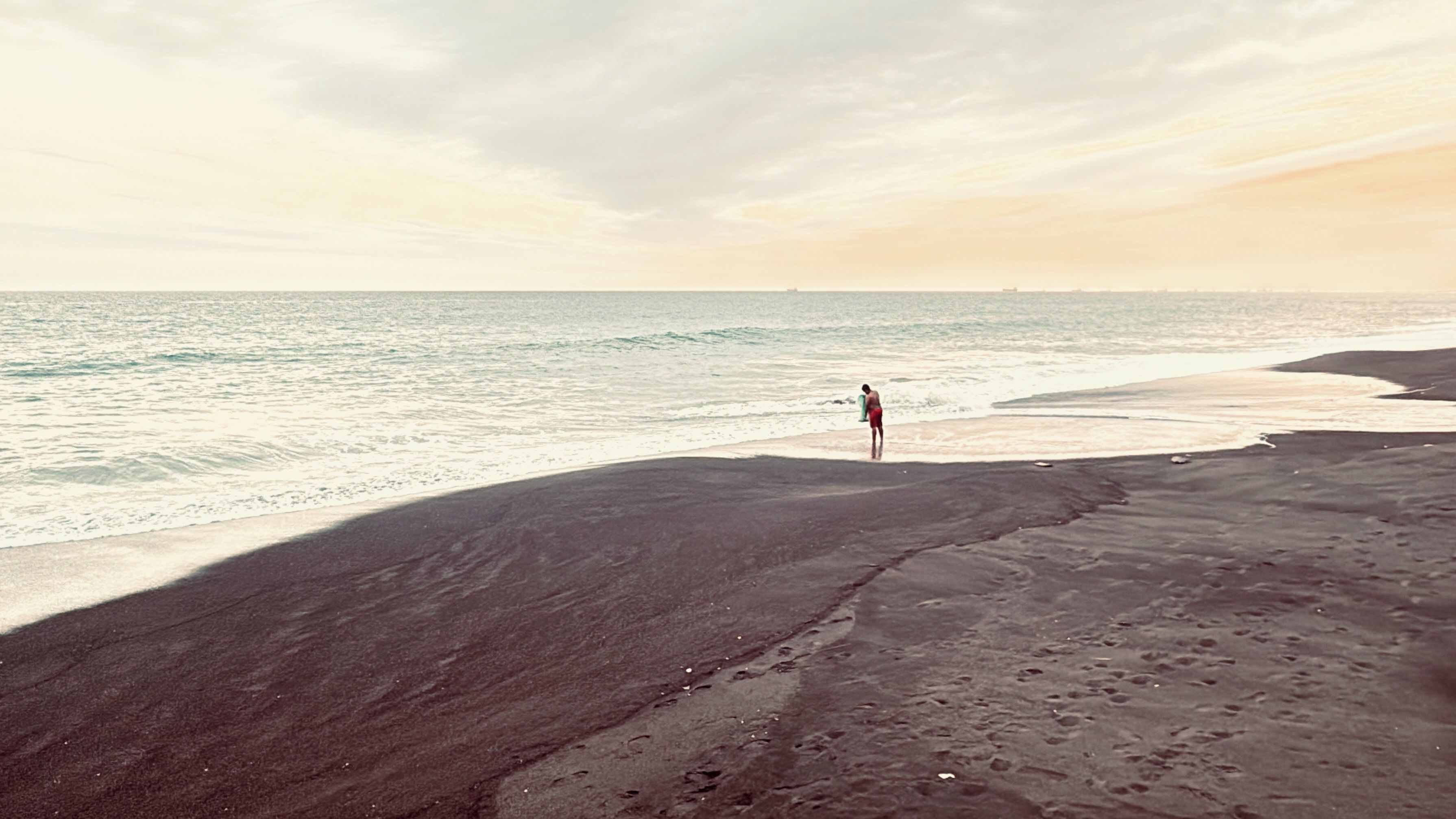 Una playa con una persona de pie sobre la arena cerca del agua.
