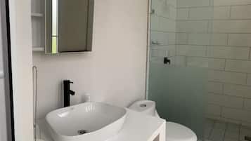 Une salle de bain avec un lavabo blanc, des toilettes et une douche à parois de verre.