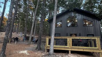A cabin with a wooden deck, large windows, and a forested backdrop.