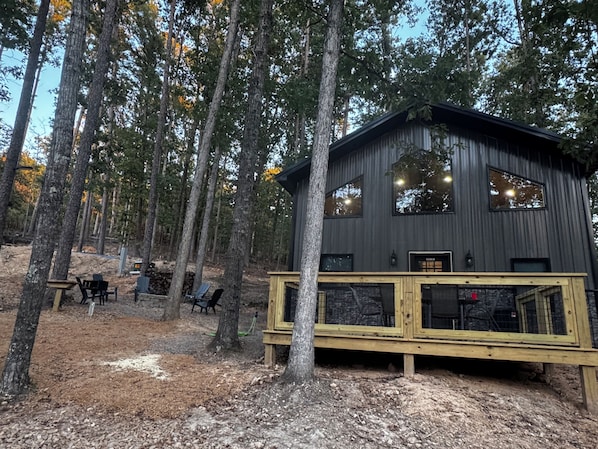 A cabin with a wooden deck, large windows, and a forested backdrop.