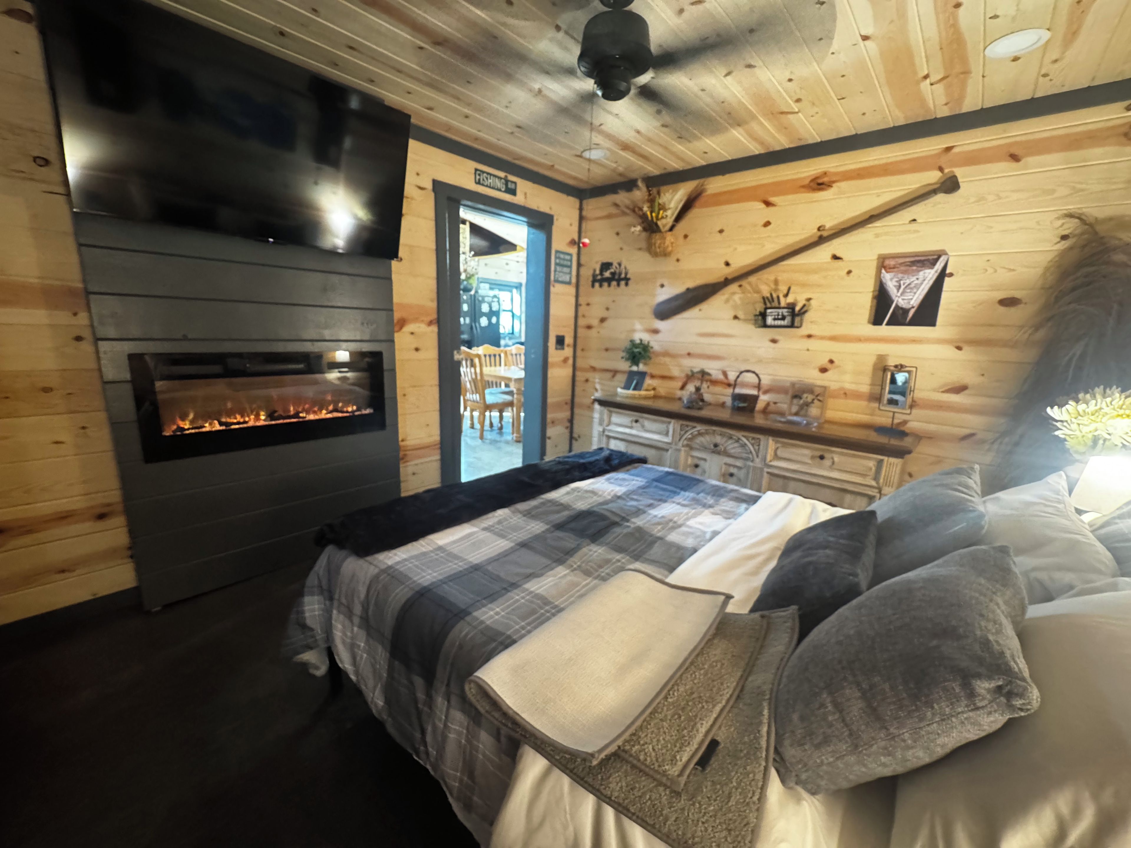 A cozy room with a fireplace, a bed with a plaid blanket, and a wooden wall with a sign indicating a fishing area.