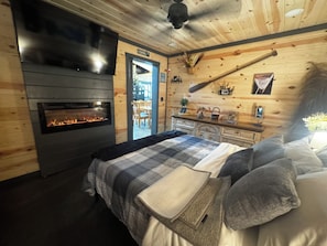 A cozy room with a fireplace, a bed with a plaid blanket, and a wooden wall with a sign indicating a fishing area.