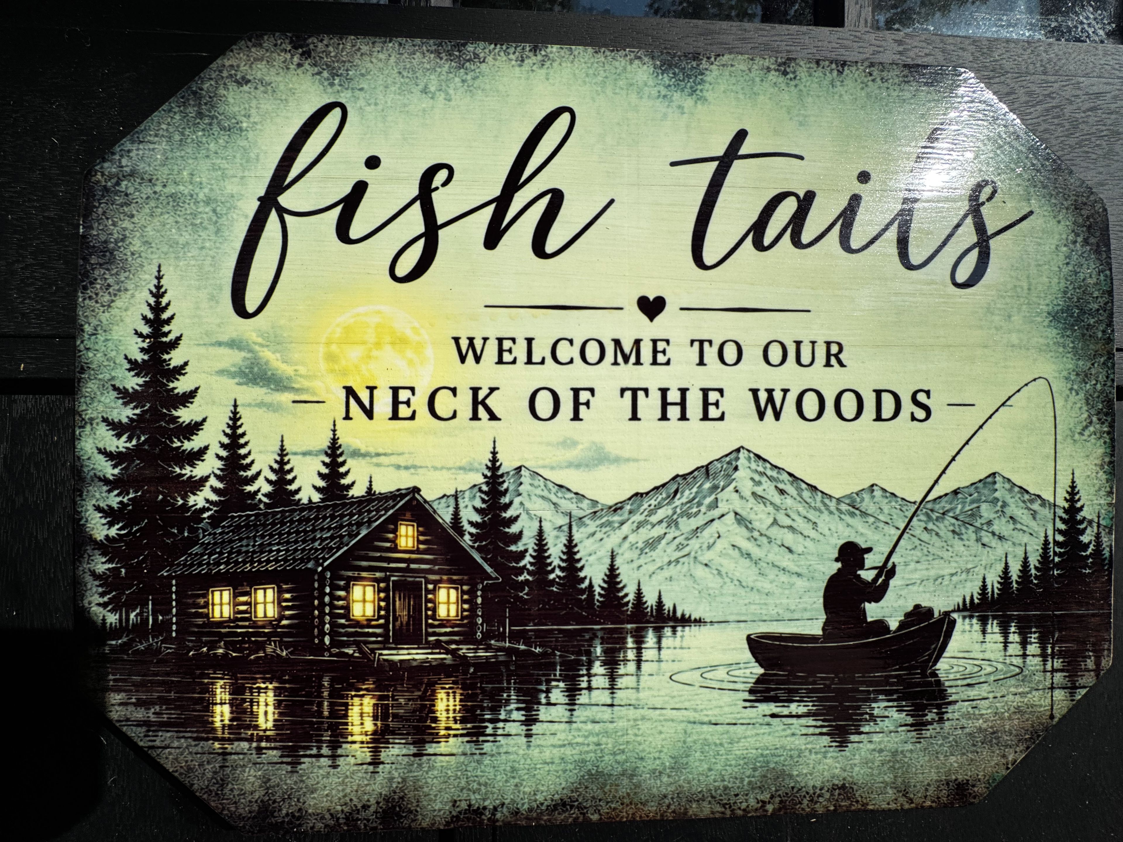 A welcome sign for a cabin area with a fishing theme, featuring a cabin, a person fishing, and a mountain backdrop.