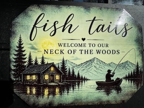 A welcome sign for a cabin area with a fishing theme, featuring a cabin, a person fishing, and a mountain backdrop.