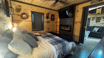 Une chambre confortable dans un chalet, avec un lit, une cheminée et un téléviseur fixé au mur.