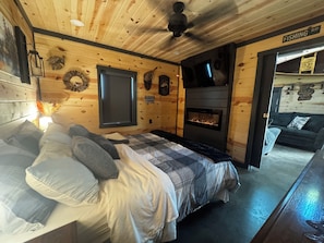 A cozy cabin room with a bed, a fireplace, and a television mounted on the wall.