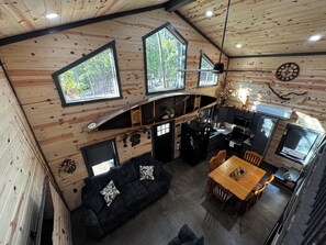 Interior de una cabaña con comedor, cocina y sofá con cojines decorativos.