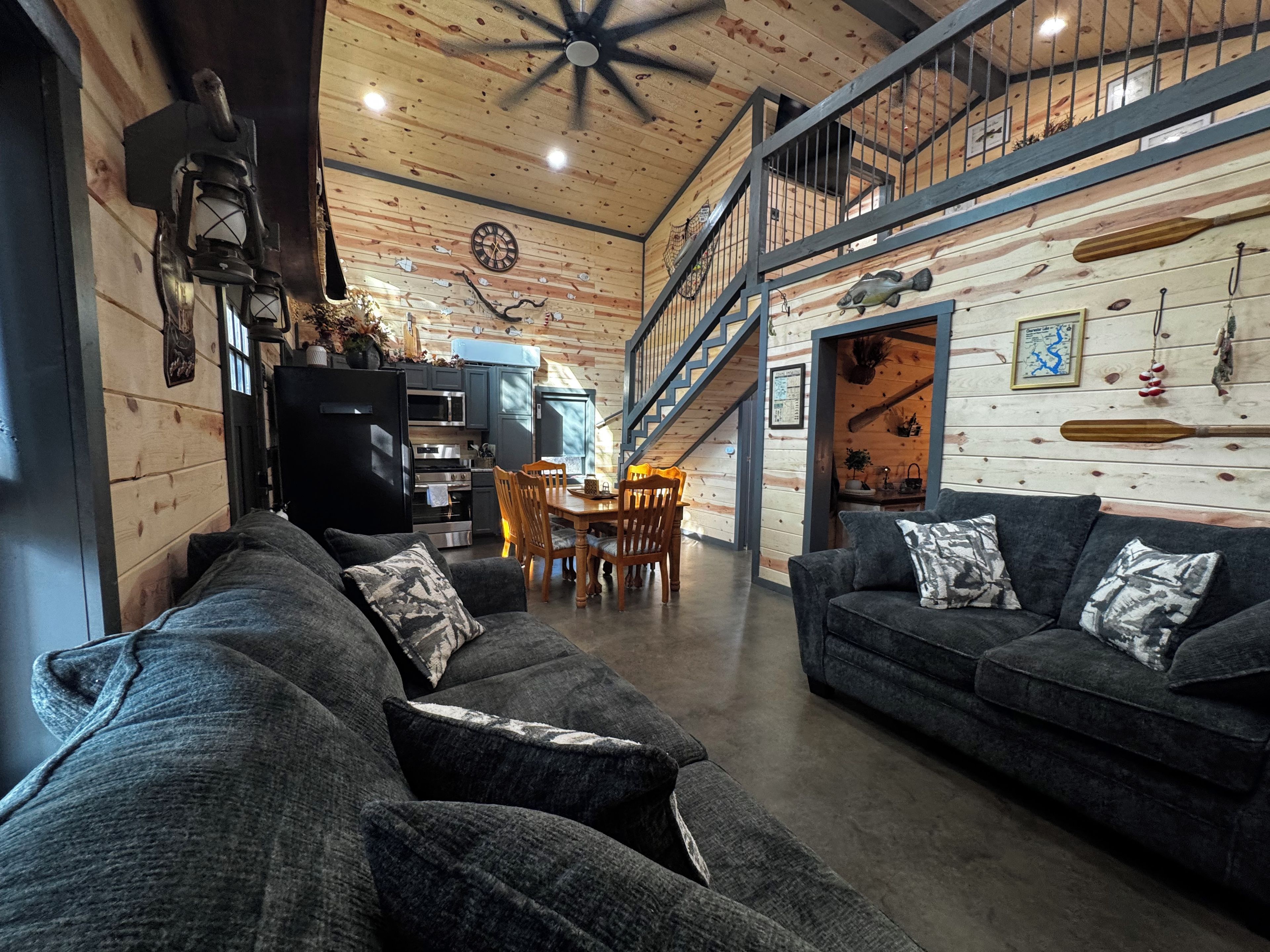 A spacious living area with a high ceiling, a dining table with chairs, and a staircase leading to an upper level.