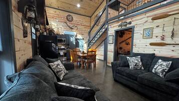 A spacious living area with a high ceiling, a dining table with chairs, and a staircase leading to an upper level.