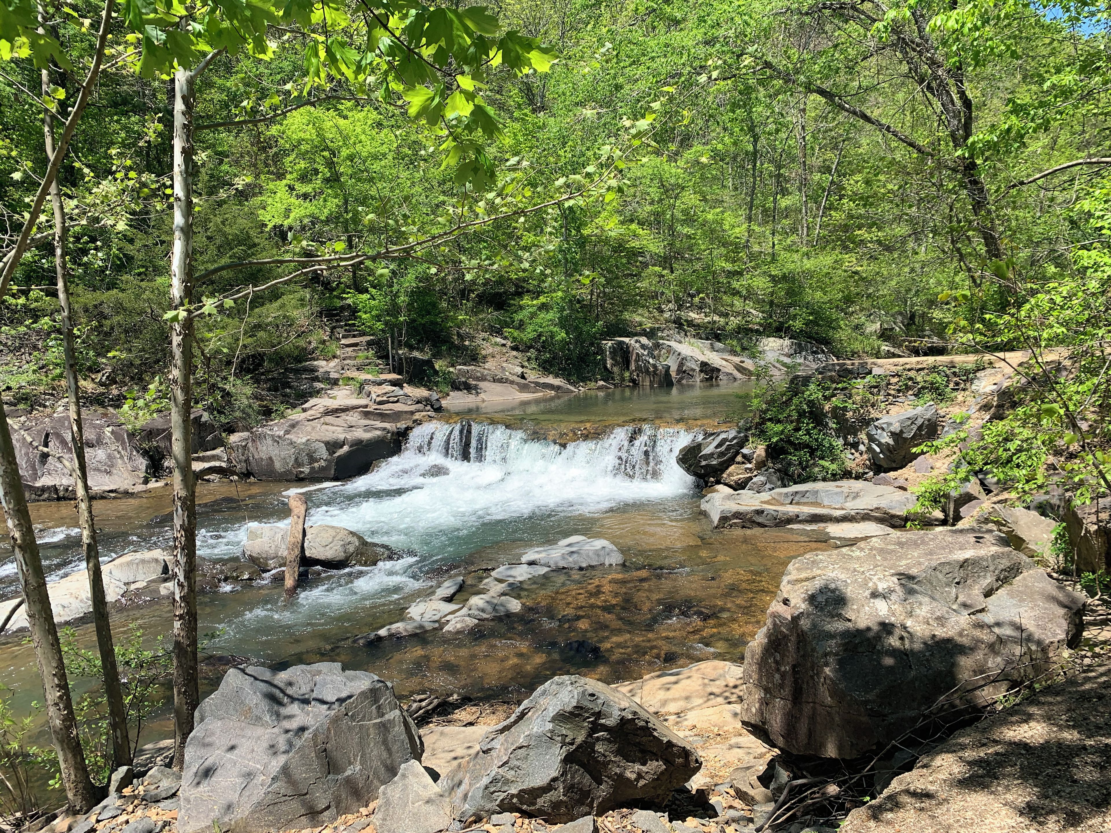 Paesaggio naturale con una cascata, terreno roccioso e vegetazione lussureggiante.