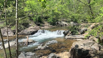 Paesaggio naturale con una cascata, terreno roccioso e vegetazione lussureggiante.