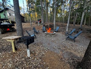 An outdoor seating area with Adirondack chairs, a fire pit, and a grill.