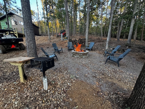 An outdoor seating area with Adirondack chairs, a fire pit, and a grill.
