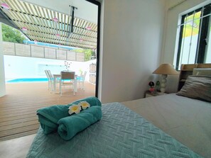 A hotel room with a bed, a nightstand, a lamp, and a view of an outdoor pool area. - Villa Palmito: 3-room Villa with a Private Pool in Trou aux Biches (Trou aux Biches)