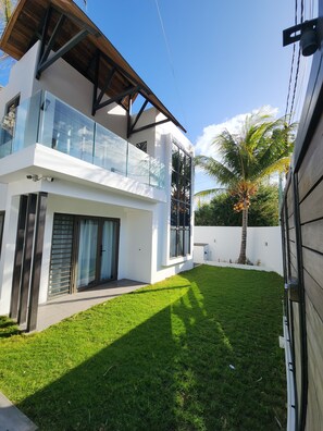 Ein modernes, zweistöckiges Haus mit Glasbalkon, gepflegtem Rasen und einer Palme.