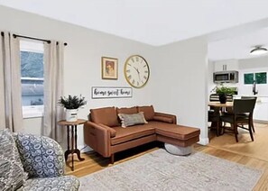 A modern living room with a brown sectional sofa, a small side table, a clock, and a sign on the wall.